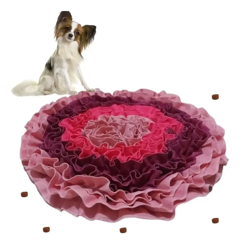 Tapete de fuçar redondo com tiras de tecido em tons de rosa e vinho, com petiscos espalhados e um cãozinho papillon ao fundo